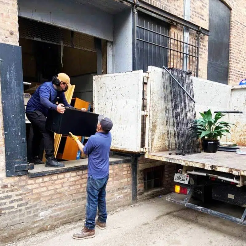 Two junk removal specialists offering furniture removal services to move bulky items from the building's freight elevator to the junk removal truck in a chicago alley | Junk Relief