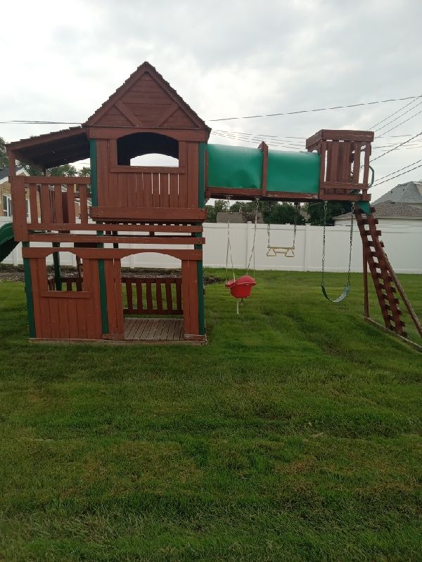 Before: two-tower wooden playset with tube slide, swings and rock wall